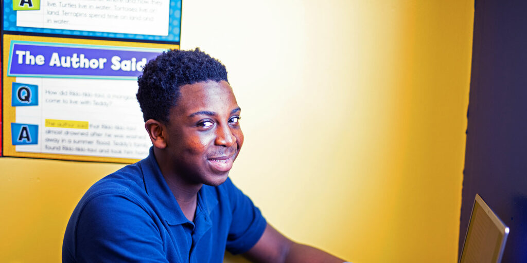 Middle school student smiling in classroom while working on computer that their desk.